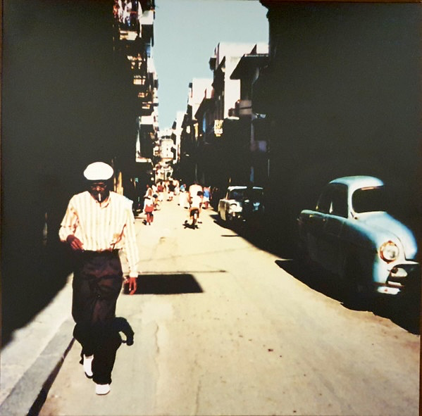 Buena Vista Social Club - Cover art with a Man walking down a city street with vintage cars on a sunny day