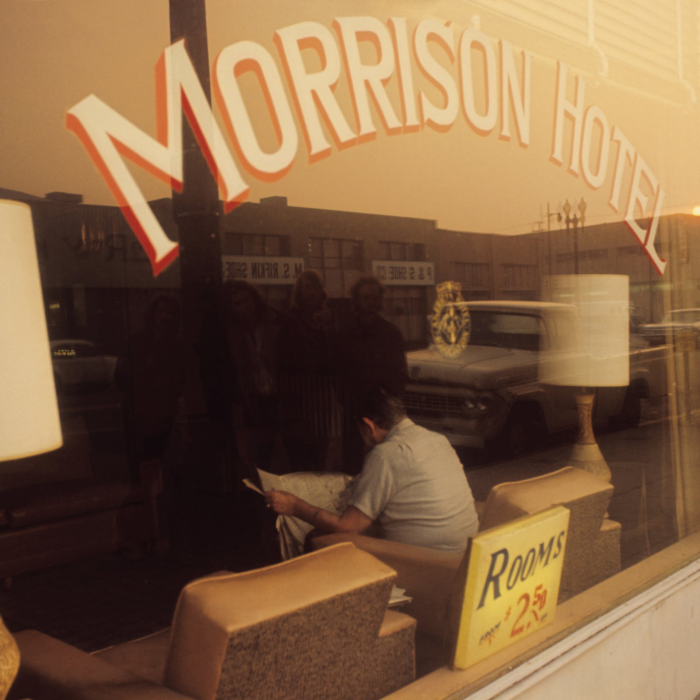 A person sitting in a room with a window viewing the outside of the Morrison Hotel. Cover art for Morrison Hotel Sessions double vinyl by The Doors