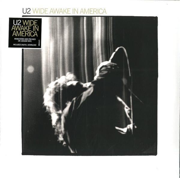 U2 - Wide Awake In America album cover, featuring a black and white photo of the band performing on stage with a visible microphone and the album title text.