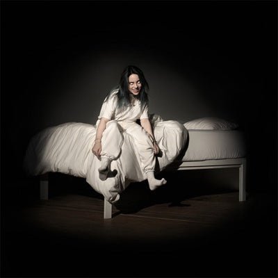 Billie Eilish sitting on a bed in a dimly lit room, wearing a white outfit and a white hat, with her feet up on the bed.